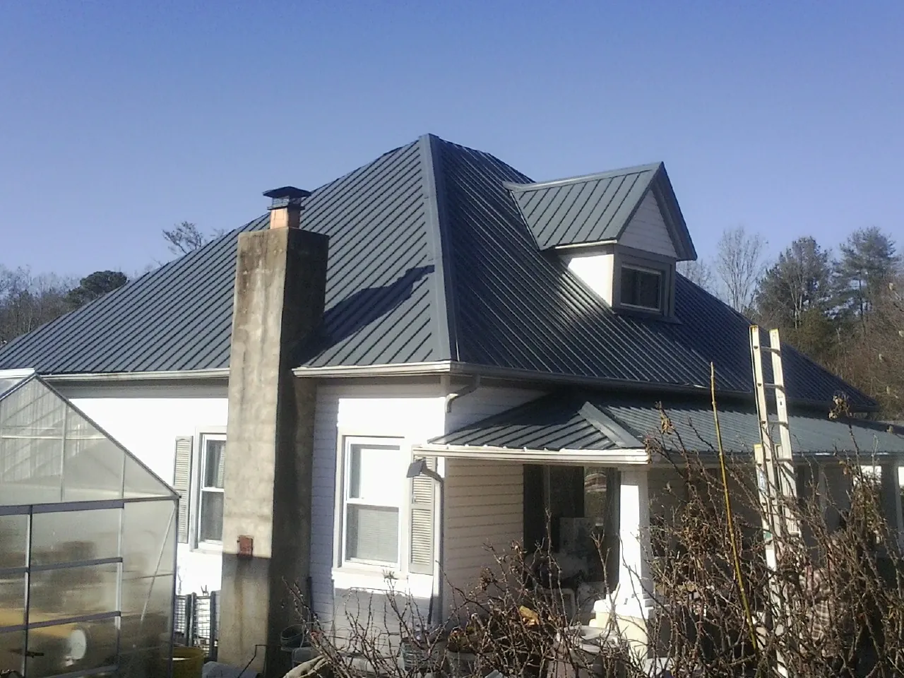 Dark blue standing seam metal roof on a white farmhouse with dormer — Slate & Tile Roof Repair by Roofing Brothers in Lucernemines