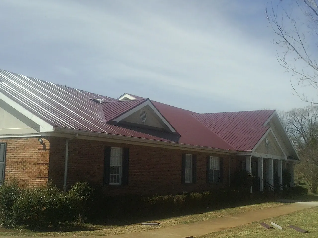 Red metal roof with gabled entries on a long brick building, from a Hail Damage Roof Repair job in Lucernemines
