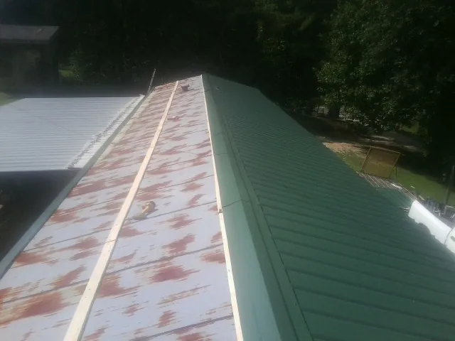 Old rusted panels beside newly installed green metal roofing — Wind Damage Roof Repair by Roofing Brothers in Lucernemines