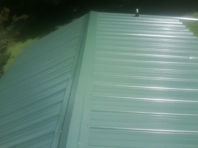 New green metal panels meeting at the ridge of a roof — Flat Roof Repair work by our crew in Lucernemines