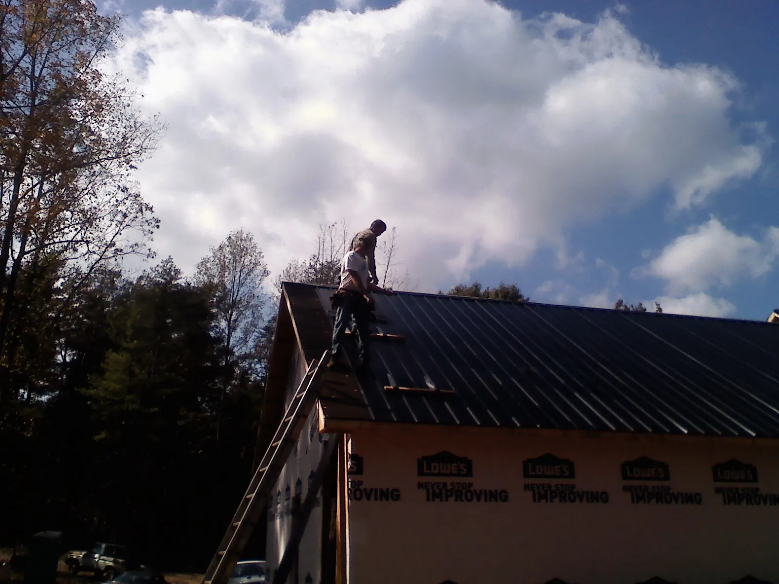 Roofer fastening dark metal panels high against a cloudy sky, from a Roof Inspection job in Lucernemines