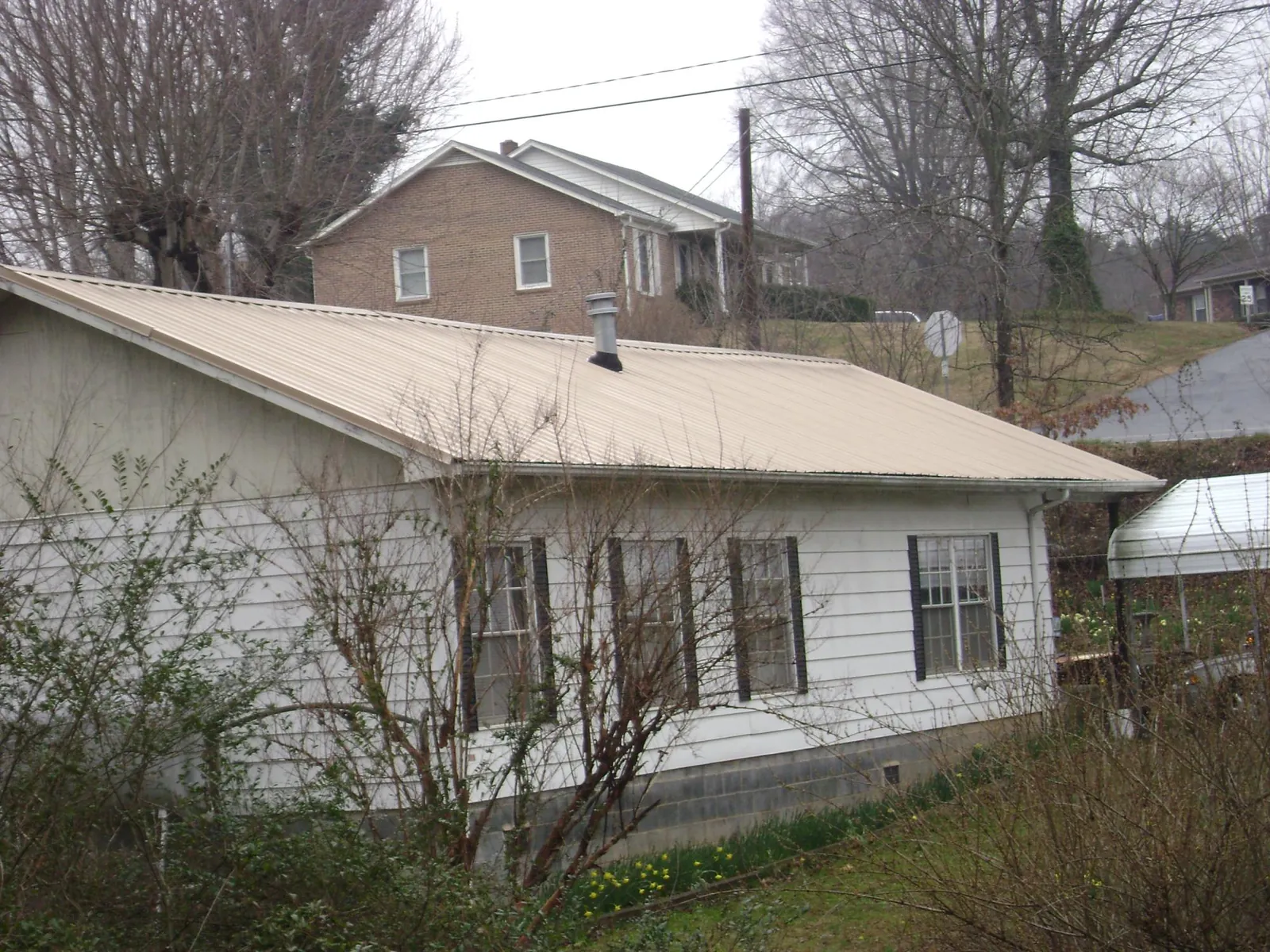 Tan metal roof on a white sided house set into a hillside — Commercial Roofing by Roofing Brothers in Lucernemines