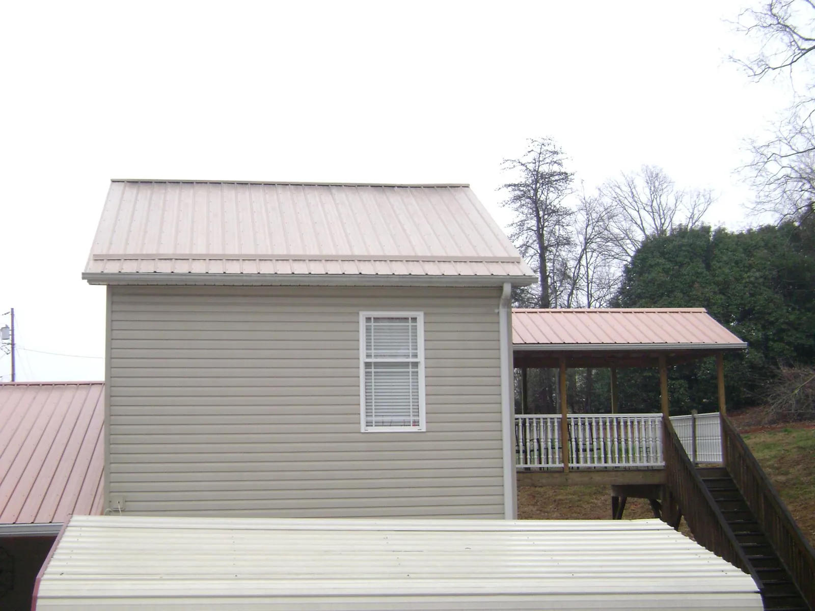 Tan metal roofs on a two story addition and attached porch, from a Roof Replacement job in Lucernemines